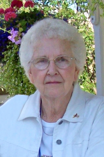 Burdine Hofbauer, wearing white, poses in front of garden flowers.