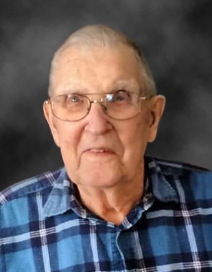 Glen Mabus looks up at the camera. He is wearing a blue plaid shirt and gold-rimmed glasses.