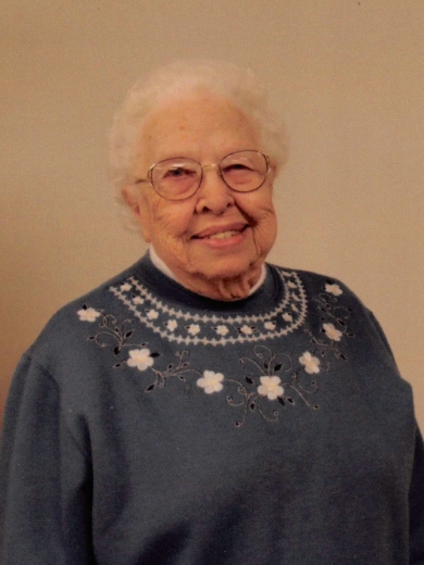 Jennie smiles warmly. She wears a blue sweater with embroidered flowers.