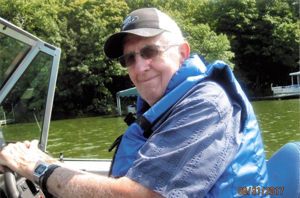 Richard smiles gently. He is driving a boat on green, still waters.