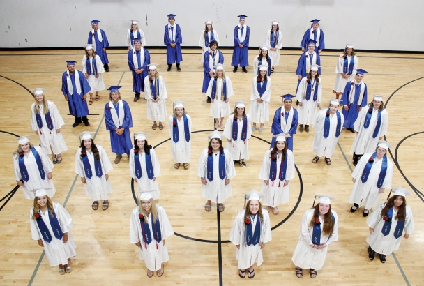 The class of 2020 in blue and white regalia stands spaced apart in the North Iowa gymnasium.
