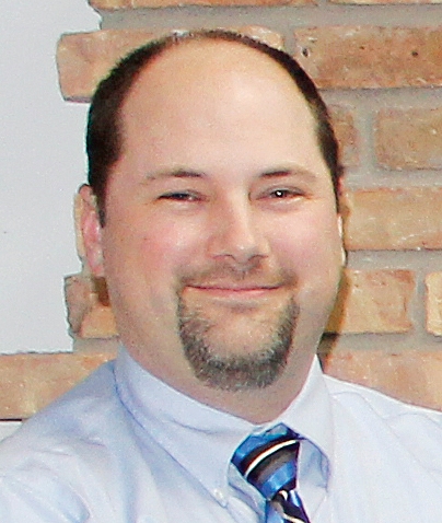 Joe Erickson smiles, wearing a blue shirt and tie.
