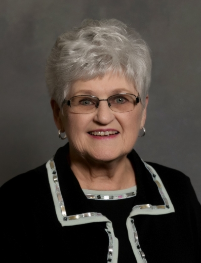 Donna smiles, wearing a matching black blouse and jacket in front of a gray backdrop.